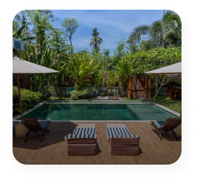 image of an outdoor swimming pool surrounding by greenery, lounging deck and two sun chair in front of pool and blue sky 